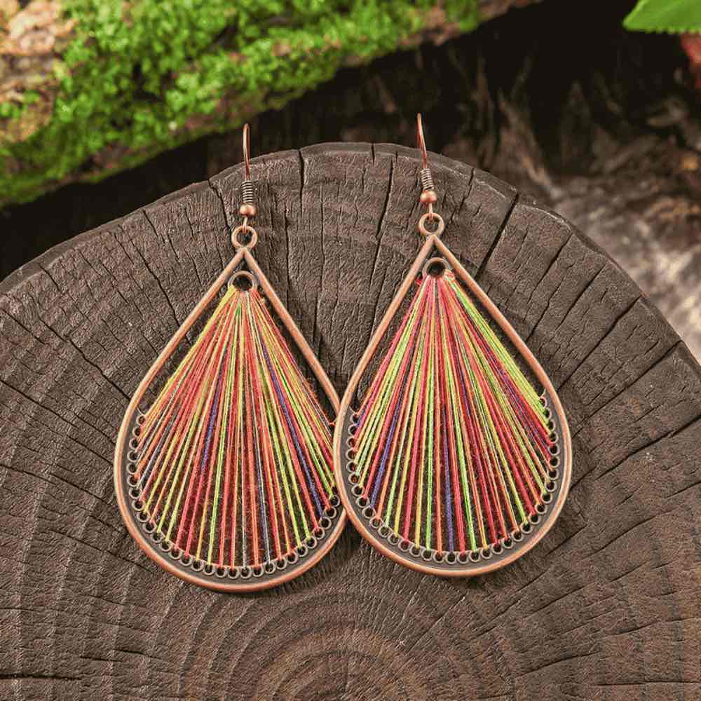 Multicolor threaded boho earrings with a copper-toned frame, resting on a rustic wooden surface.
