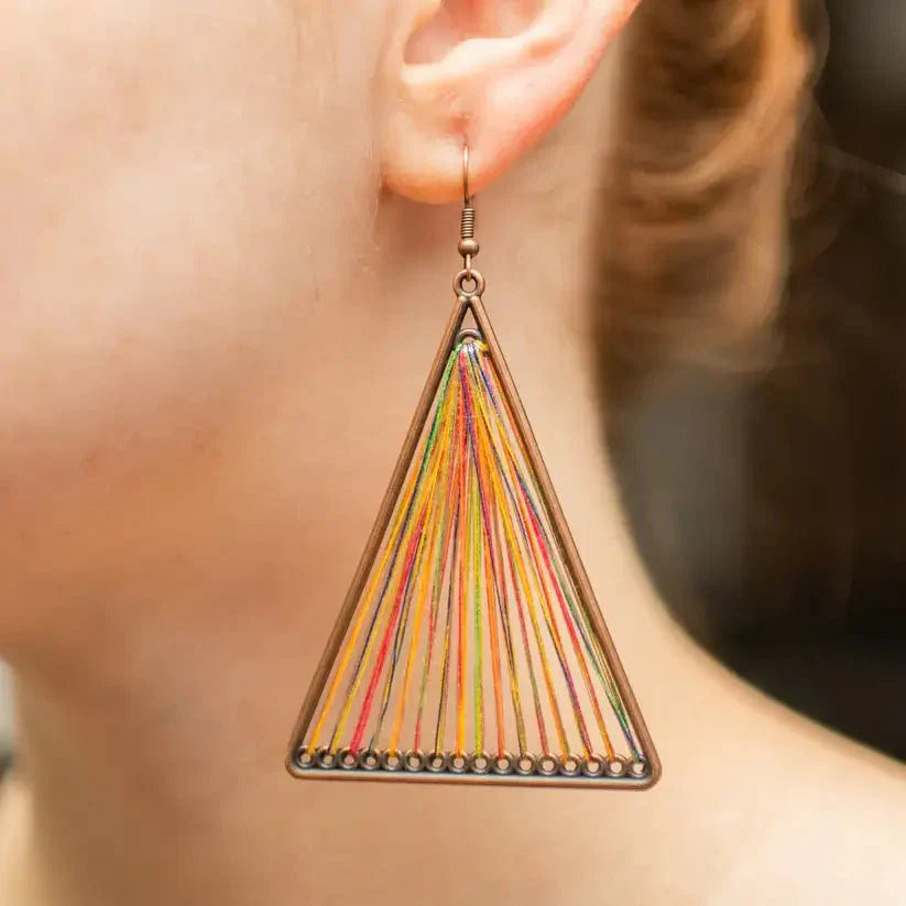 Close-up of a model wearing a single boho earring, showcasing the large bronze triangle frame with vibrant multicolor threads.