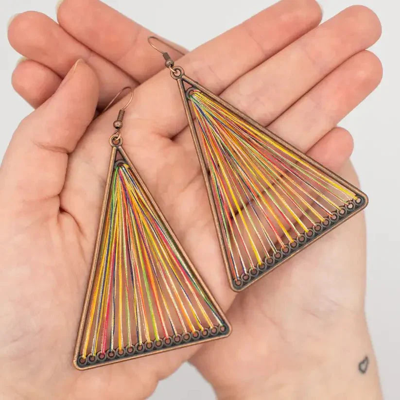 Two boho earrings held in hands, highlighting the intricate multicolor string art within the bronze geometric triangle frames.