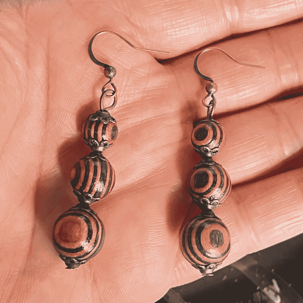 A hand holding a pair of boho wooden beaded drop earrings, showcasing the black and brown striped and swirl patterns on the beads.