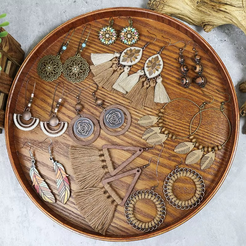 An overhead view of a wooden tray filled with various styles of wooden earrings, including boho earrings, tassel earrings, and geometric designs.