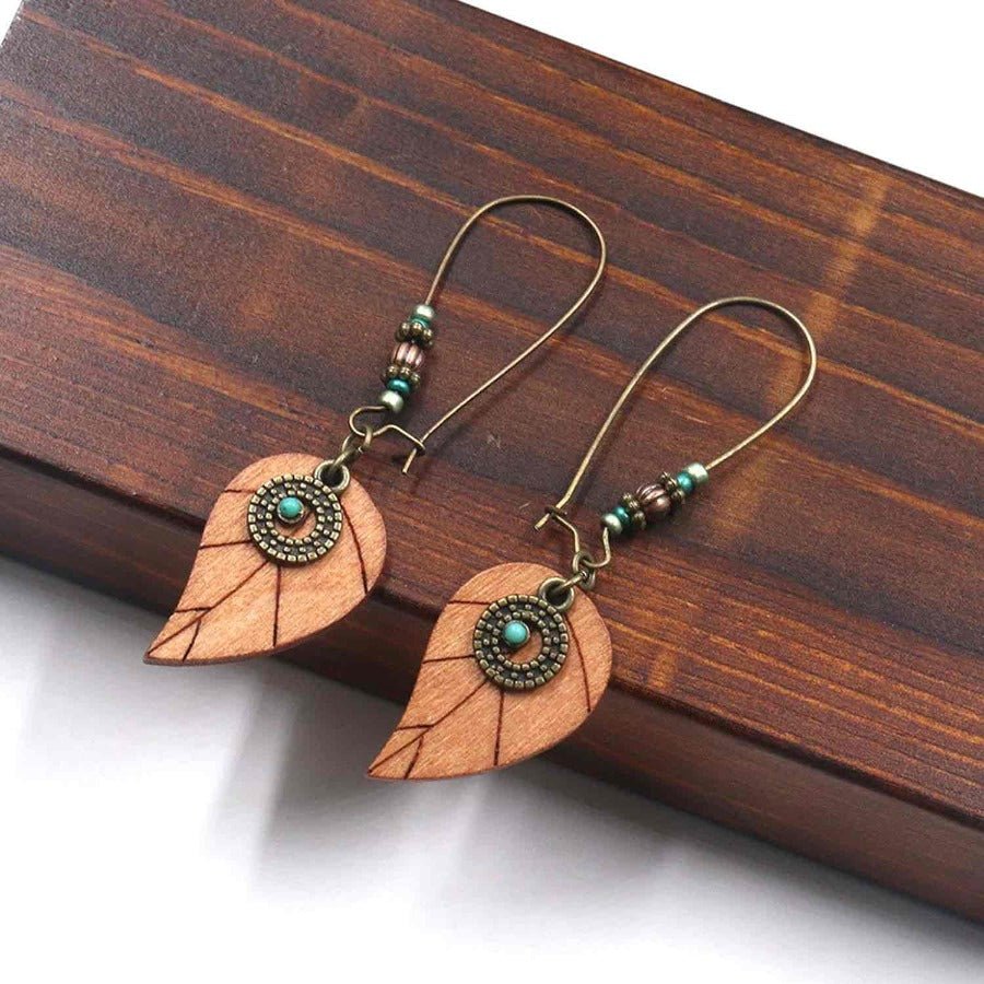 A pair of boho wooden leaf drop earrings with turquoise accents, laid on a wooden surface.
