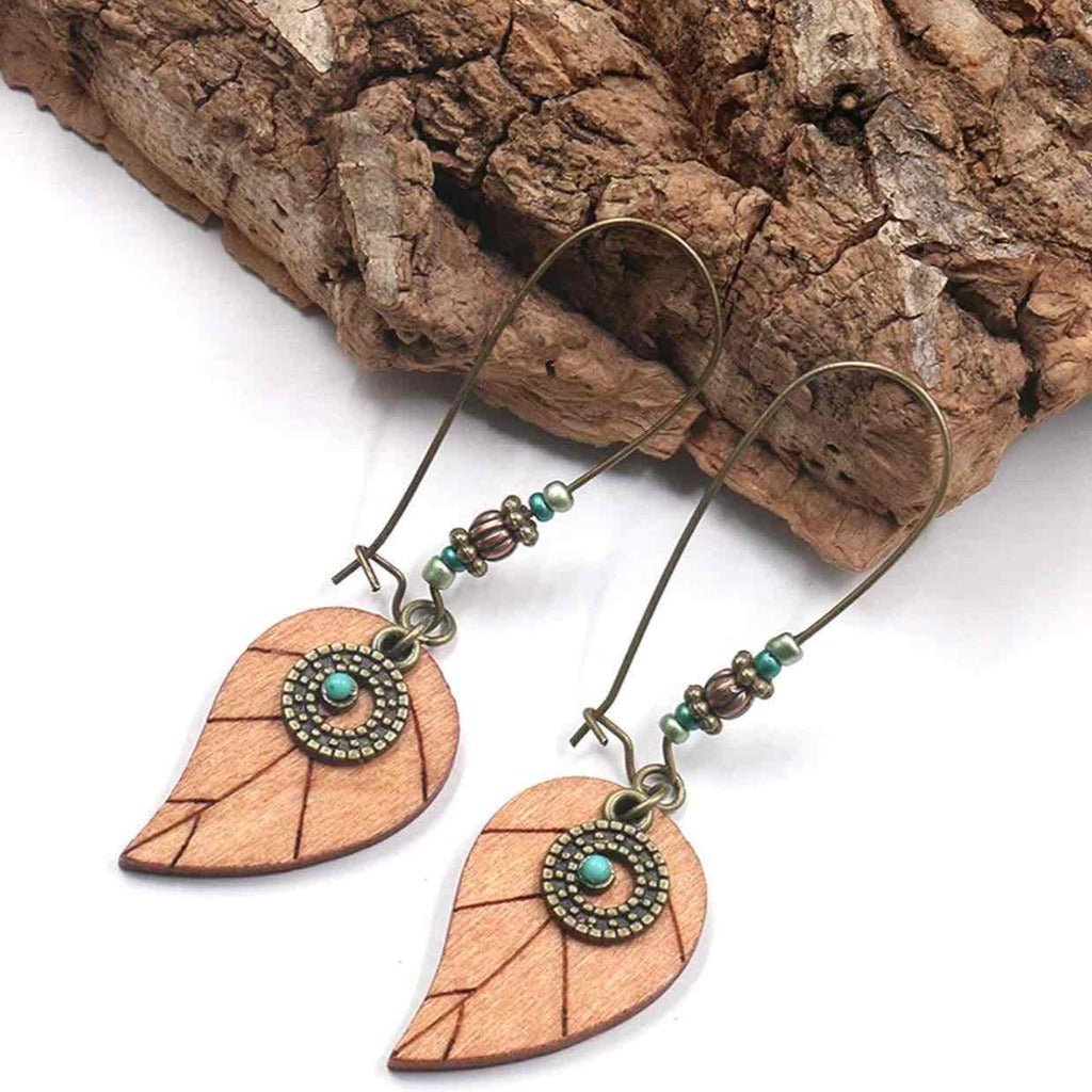 Close-up of boho wooden leaf drop earrings with turquoise accents, against a natural wood background.