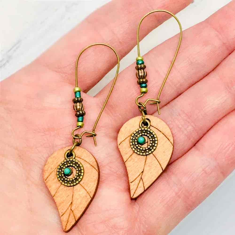 A pair of boho wooden leaf drop earrings with turquoise accents, displayed on a wooden surface.