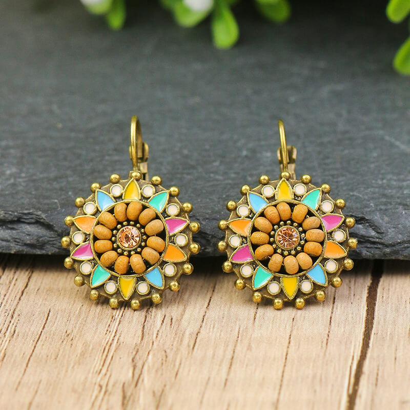A pair of boho earrings with a round, floral design featuring wooden beads, multicolor enamel, and a central stone, displayed on a dark grey surface.