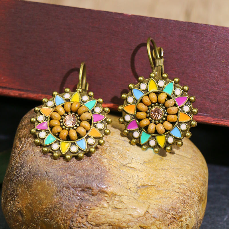 A close-up of a single boho earring, showcasing the intricate details of its round, floral design with wooden beads, multicolor enamel, and a central stone.