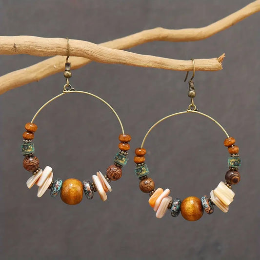 Pair of boho earrings featuring wooden beads and shell pieces on a hoop, hanging from a branch.