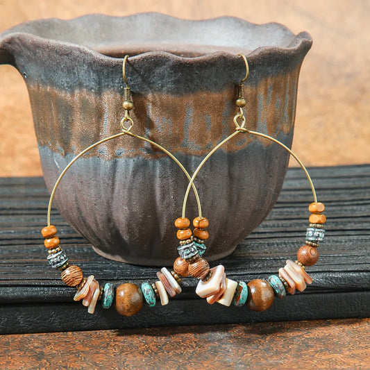 Boho earrings with wooden beads and shell accents, displayed in front of a rustic ceramic pot.