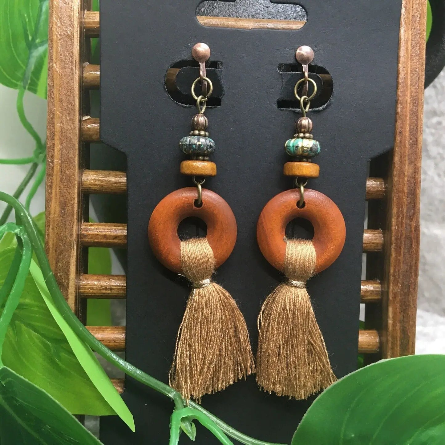 Boho wooden tassel earrings displayed on a black earring card against a wooden stand with green leaves.