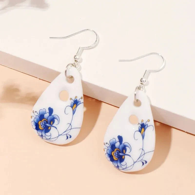 A pair of white ceramic drop earrings with blue floral designs, displayed on a light background.