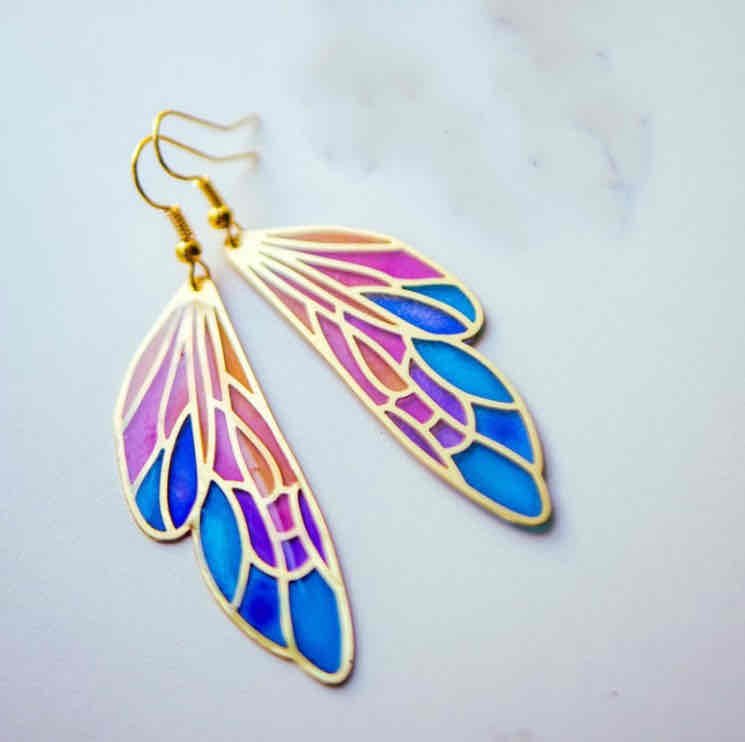 A pair of gold-tone butterfly wing boho earrings with vibrant blue, purple, and pink resin, showcasing their stained-glass effect, against a light background.