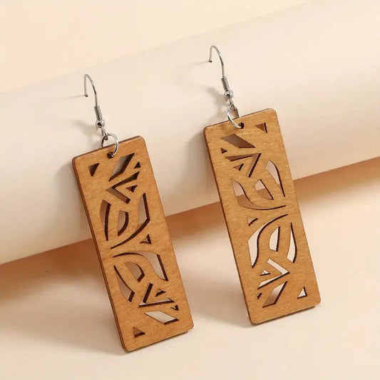 A pair of light brown wooden earrings with intricate leaf cutouts, featuring silver-toned fish hooks, against a light background.