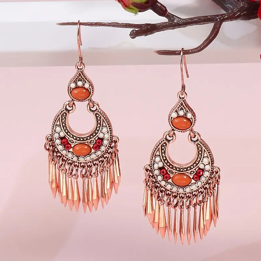 A pair of oxidised earrings with orange stones and tassels hanging against a light pink background.