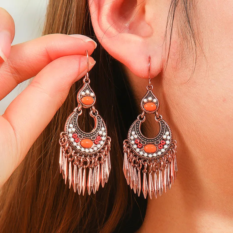 A person wearing oxidised earrings with orange stones and tassels, showcasing their size and how they look when worn.