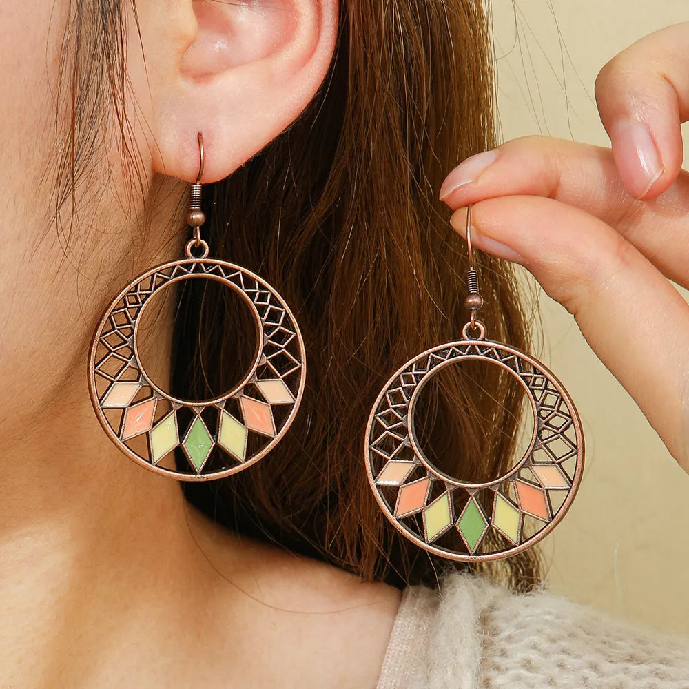 A woman wearing one of the oxidised earrings, showcasing the geometric hoop design with pastel enamel diamonds, with her hand gently touching the other earring.