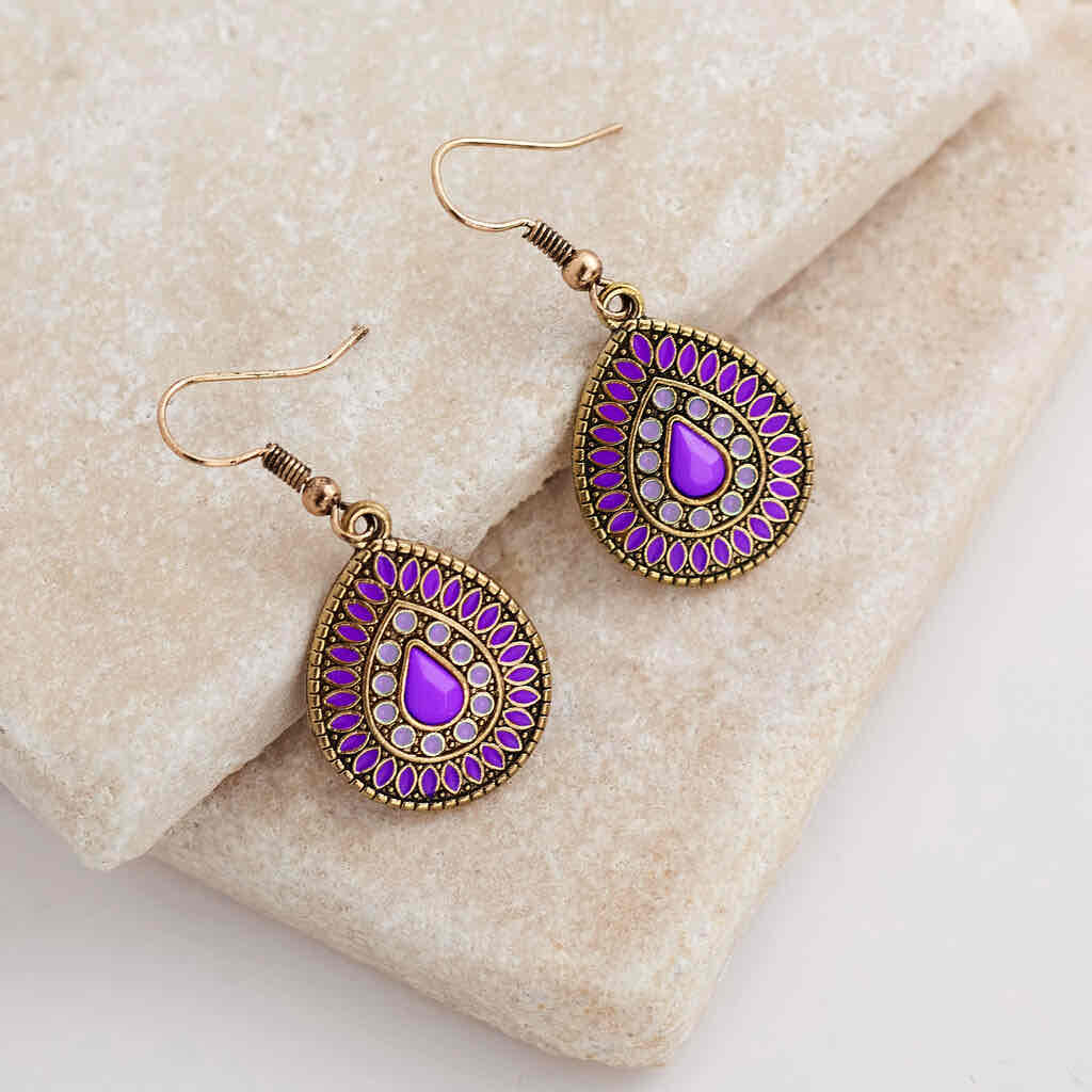 A pair of deep purple enamel teardrop drop earrings with an antique gold finish, displayed on a light-colored stone surface.
