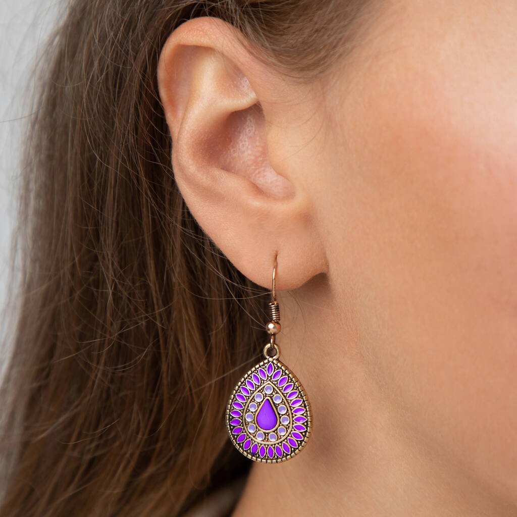 A close-up of a woman's ear wearing a deep purple enamel teardrop drop earring with an antique gold finish, showcasing its size and fit.