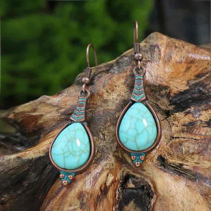 A pair of oxidised alloy teardrop turquoise stone drop earrings displayed on a rustic wooden surface, showcasing their bohemian charm.