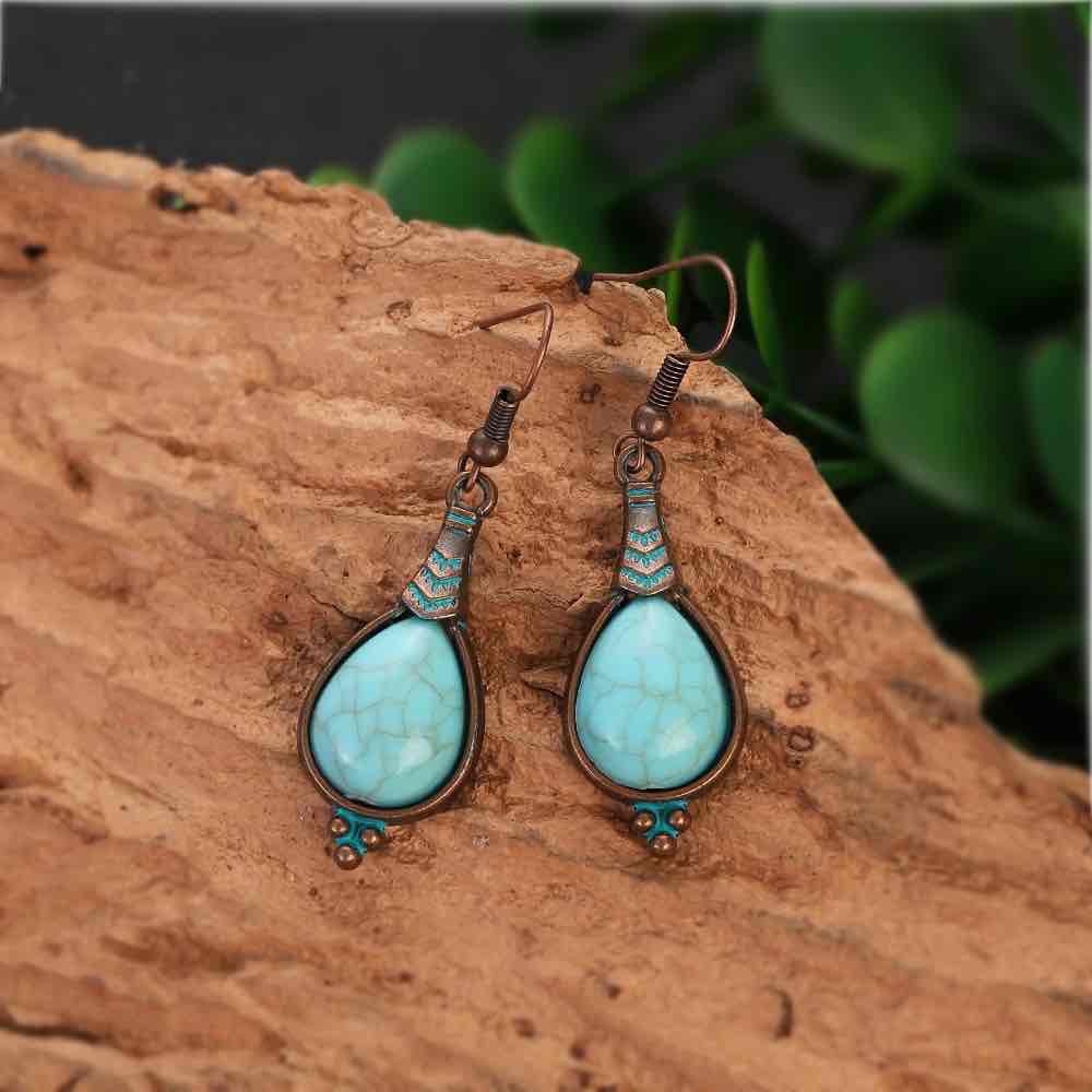 Two oxidised alloy teardrop turquoise stone drop earrings resting on a piece of wood, highlighting their intricate design and vibrant color.
