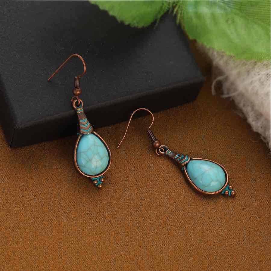 A pair of oxidised alloy teardrop turquoise stone drop earrings with a black box in the background, emphasizing their unique style.