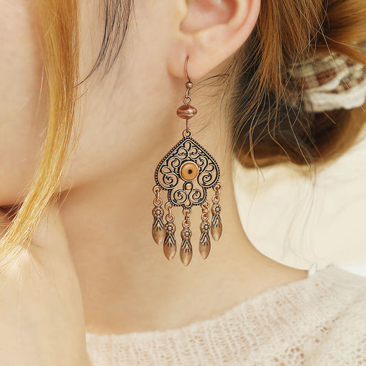 A woman wearing a single oxidised earring, showcasing its antique copper filigree design with a tan bead accent, complementing her casual attire.