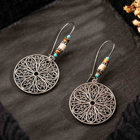 A pair of oxidised boho dangle earrings with floral filigree design and bead accents on a dark background.