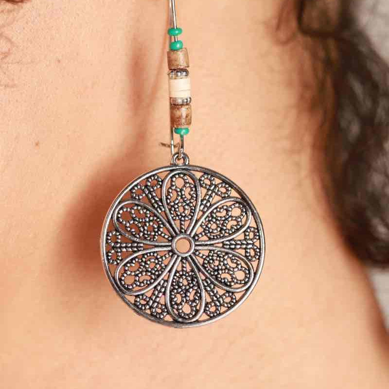 A close-up of an oxidised boho dangle earring being worn, highlighting the floral filigree design and bead accents against a person's neck.