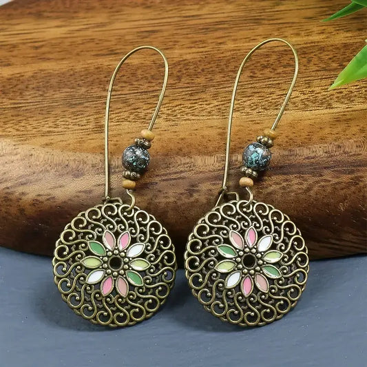 A pair of oxidised earrings with a floral medallion design and colorful beads, displayed on a wooden surface.