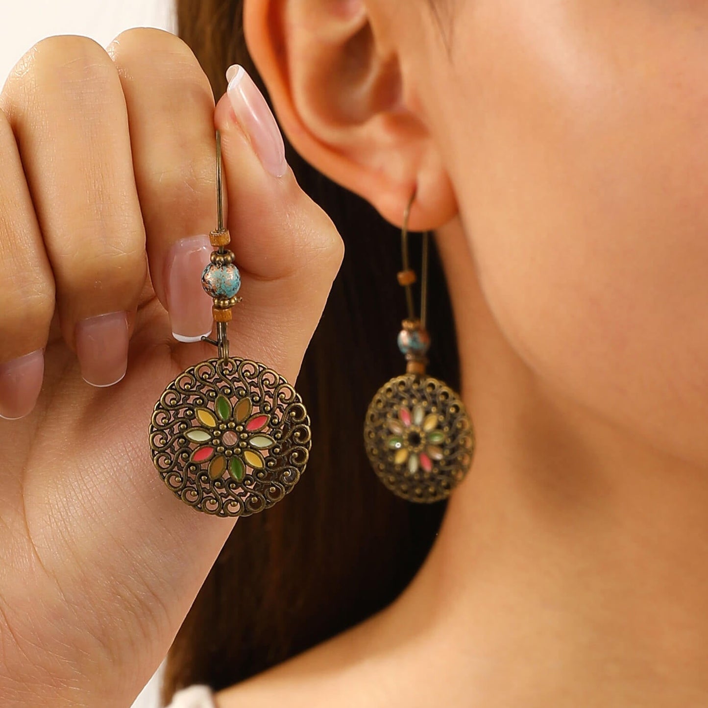 A woman holding one of a pair of oxidised earrings, showcasing the floral medallion and bead details.