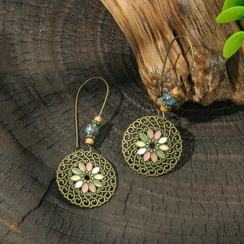 Two oxidised earrings with floral medallion designs and colorful beads, arranged on a rustic wooden background.