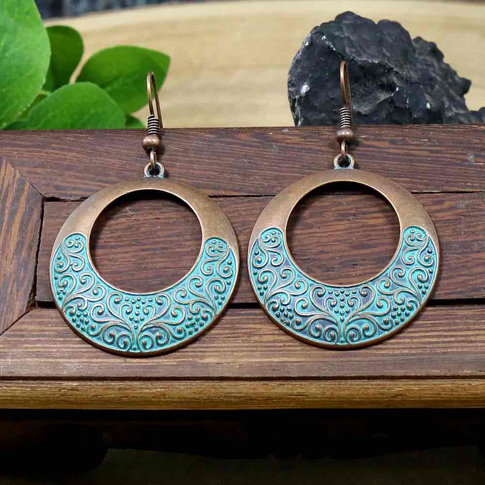A pair of oxidised boho hoop earrings with an intricate teal filigree design displayed on a wooden surface.