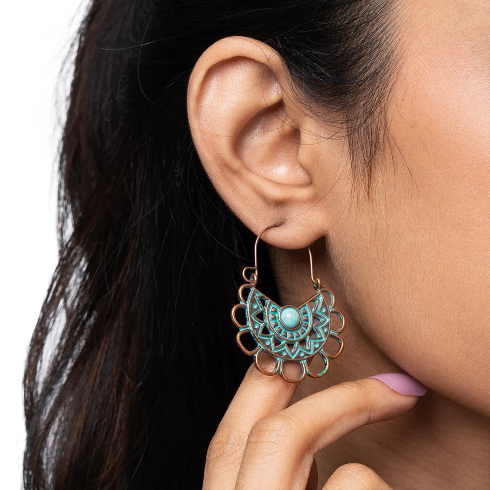 A woman wearing a single oxidised earring with a mandala design and a turquoise stone, showcasing the earring on her ear against a dark background, emphasizing the oxidised earrings.