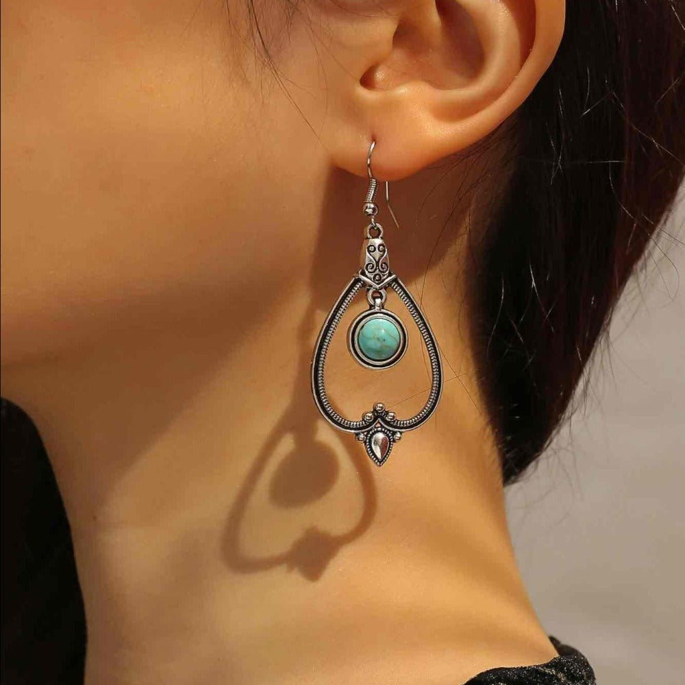 A woman wearing a single oxidised boho earring with a teardrop design and turquoise stone, showcasing its dangle.