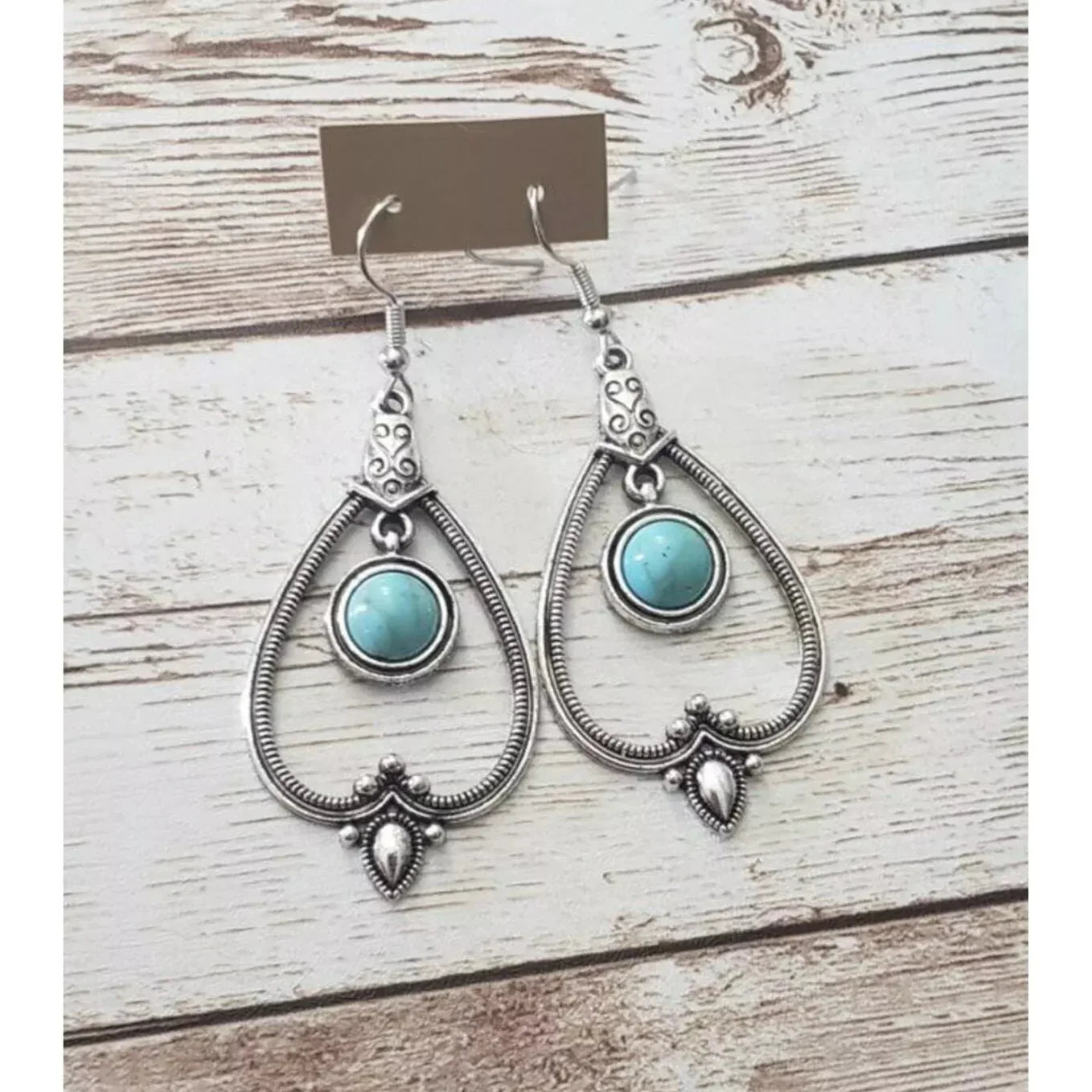 A pair of oxidised boho earrings with a teardrop shape and turquoise stone, laid flat on a rustic wooden surface.