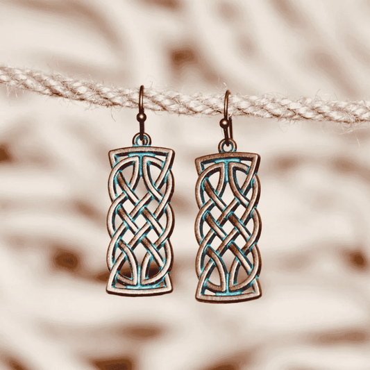 A pair of oxidised earrings with a Celtic knot design and blue patina, hanging on a rope against a blurred background.