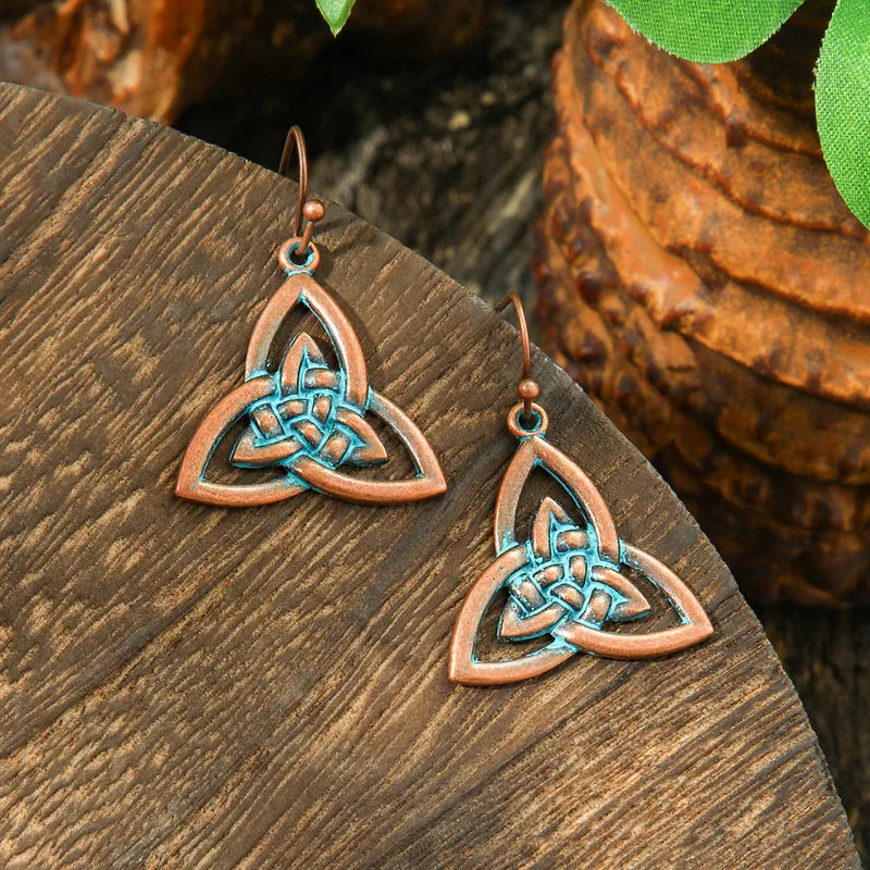 A pair of oxidised earrings with a Celtic knot design and blue patina, displayed on a wooden surface.
