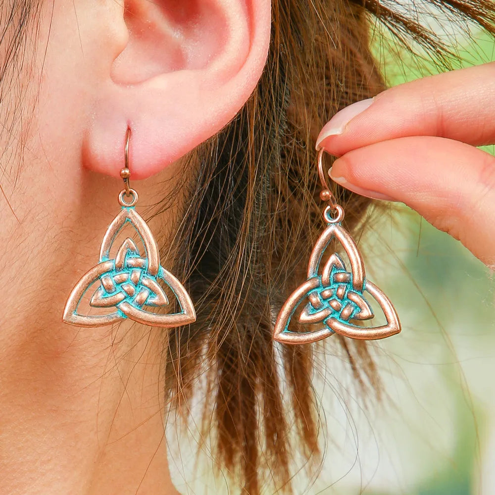 A woman wearing oxidised earrings with a Celtic knot design and blue patina, showcasing the dangle style.
