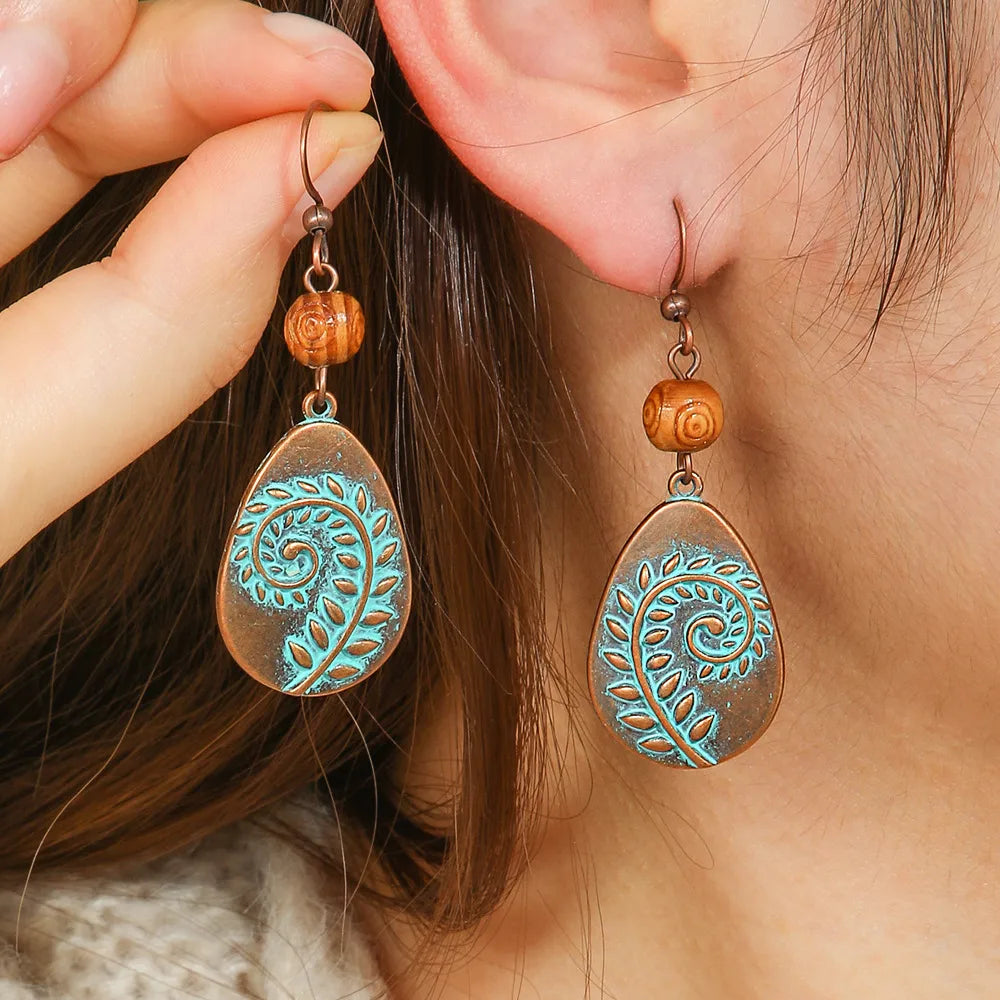 A person wearing oxidised earrings with a copper base and teal leaf swirl design, showcasing the size and fit.