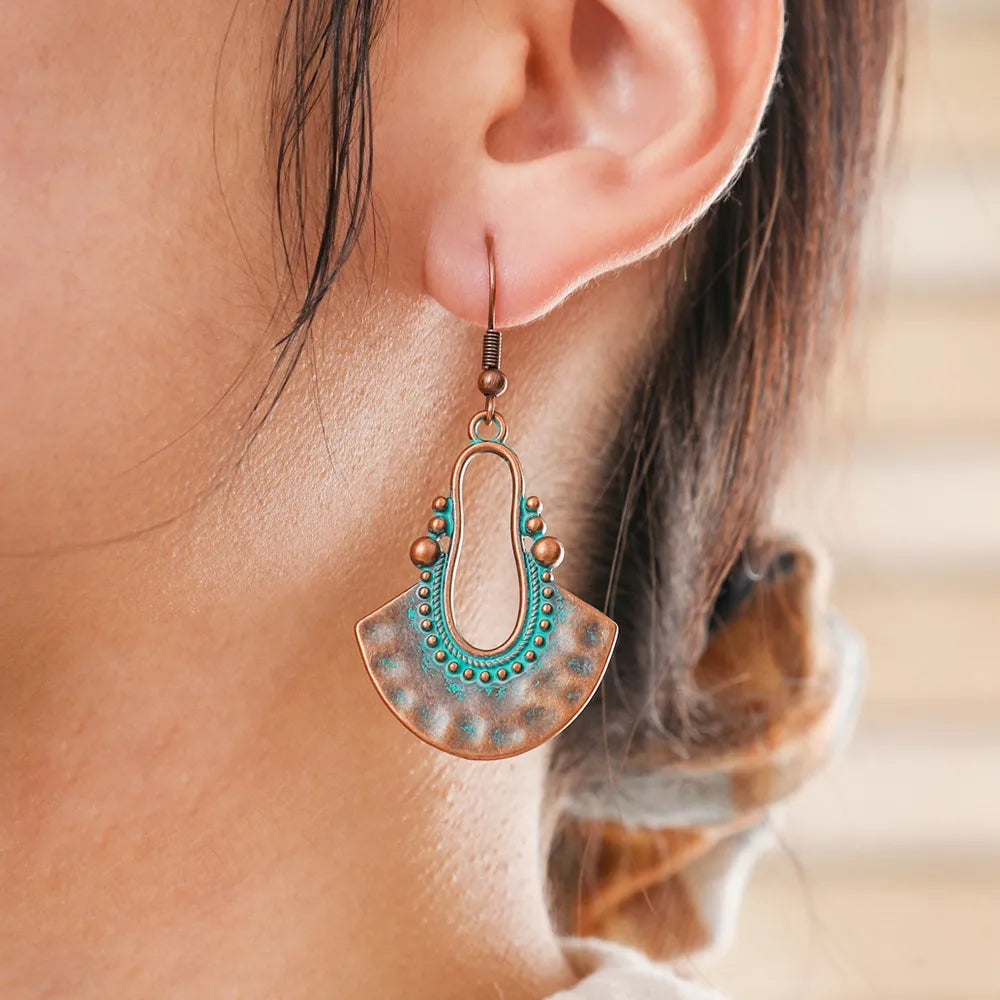 A woman wearing a single oxidised earring with a fan shape and teal patina, visible on her ear with her hair tied back.