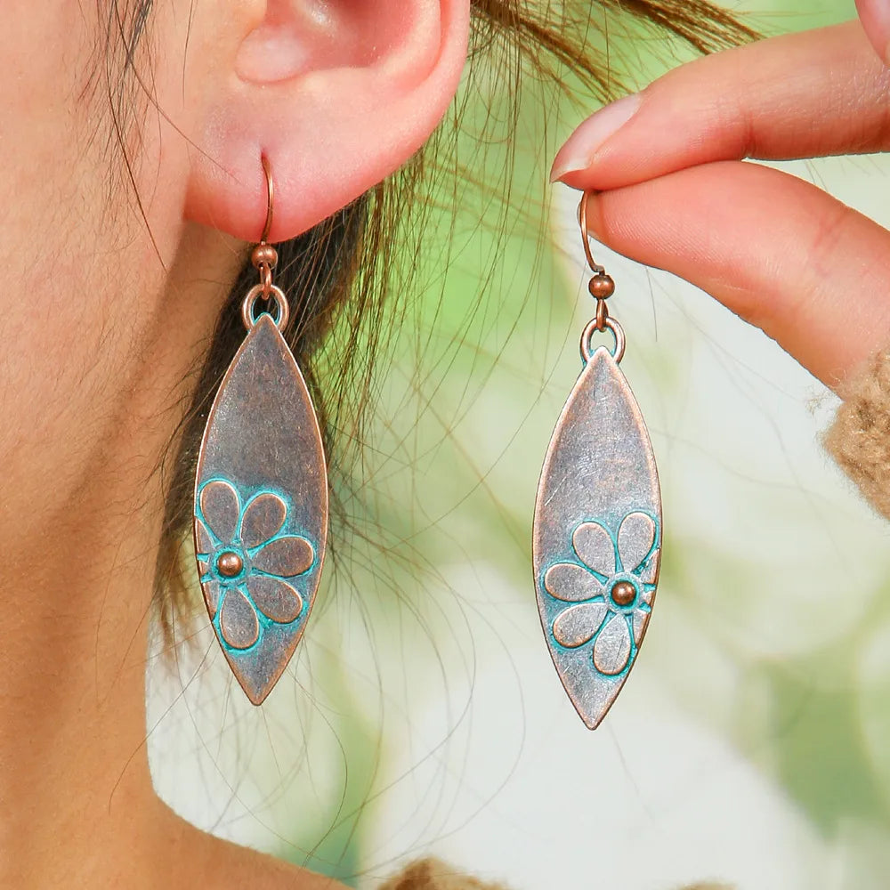 Close-up of a woman wearing oxidised earrings with a floral teal patina design, showcasing the long dangle style.