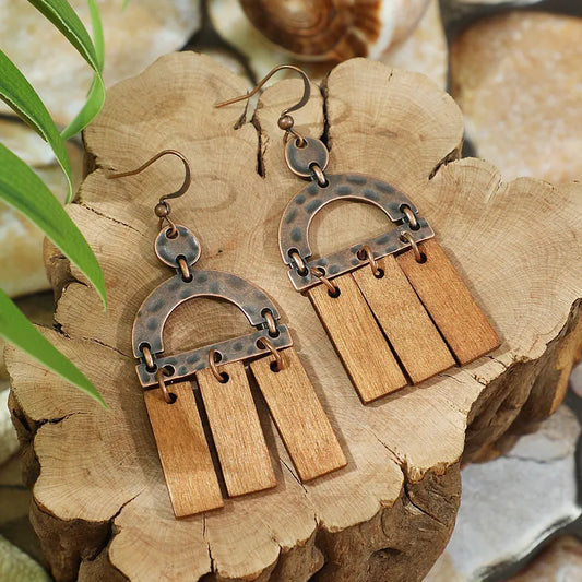 A pair of oxidised copper and wood boho earrings with an arch design, displayed on a wooden block.