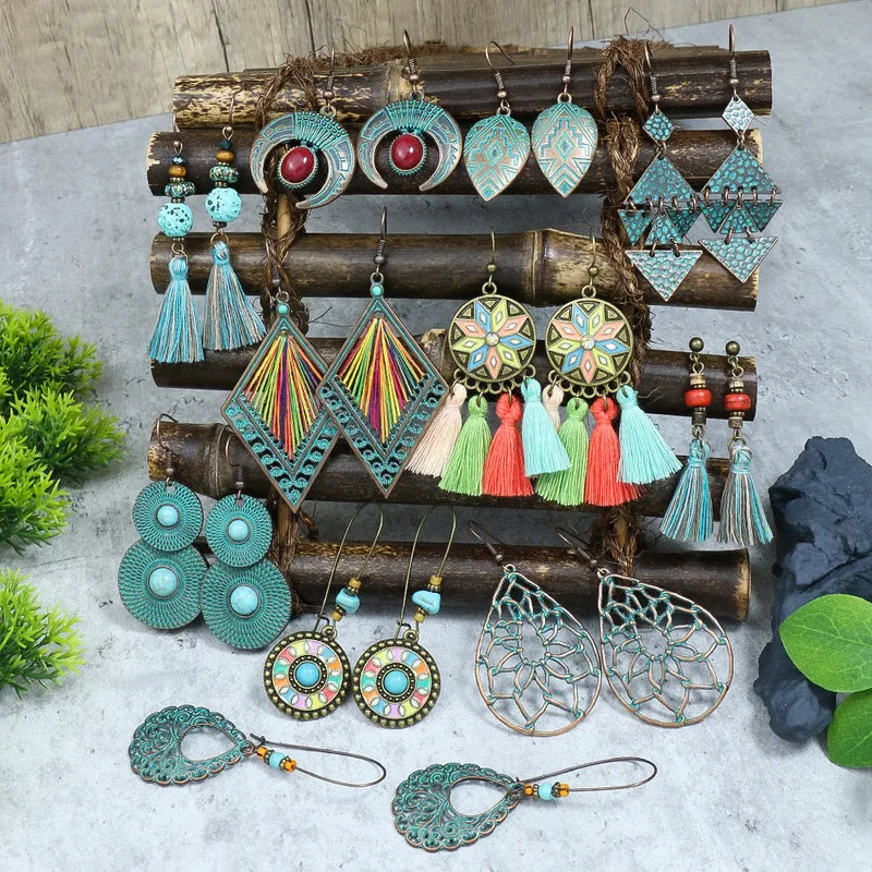 A collection of bohemian and ethnic earrings, including the featured oxidised earrings with red stone and blue patina, displayed on a wooden stand.