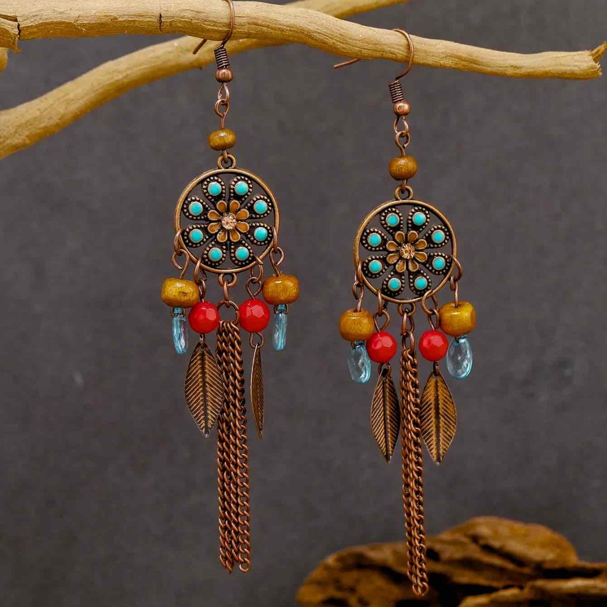 A pair of oxidised dreamcatcher long earrings with turquoise and red beads, and bronze chains, hanging from a tree branch.