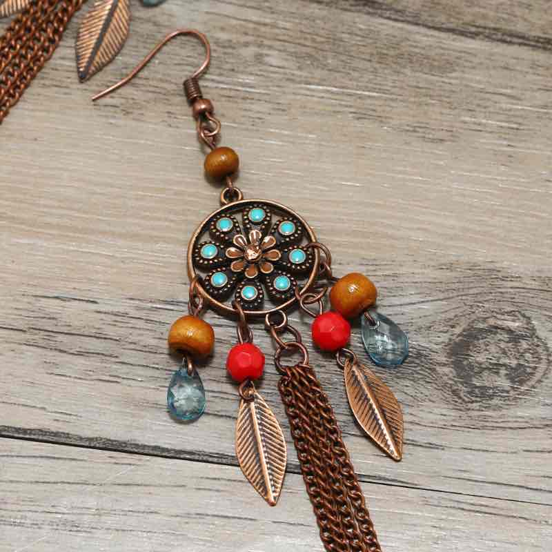 A pair of oxidised dreamcatcher long earrings with turquoise and red beads, and bronze chains, displayed on a dark background.