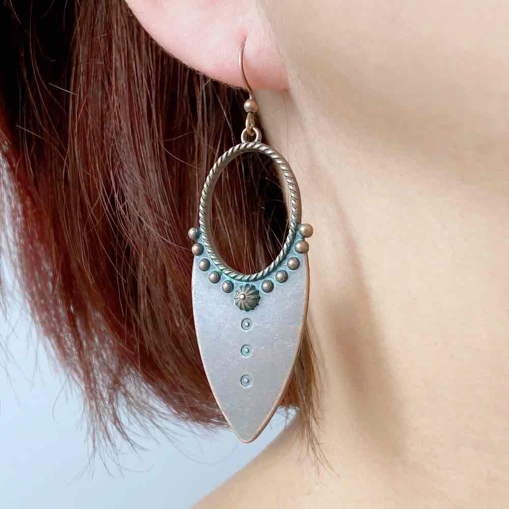 A woman wearing a single oxidised earring with teal accents, showcasing its drop design and dual-tone finish against her ear and hair.