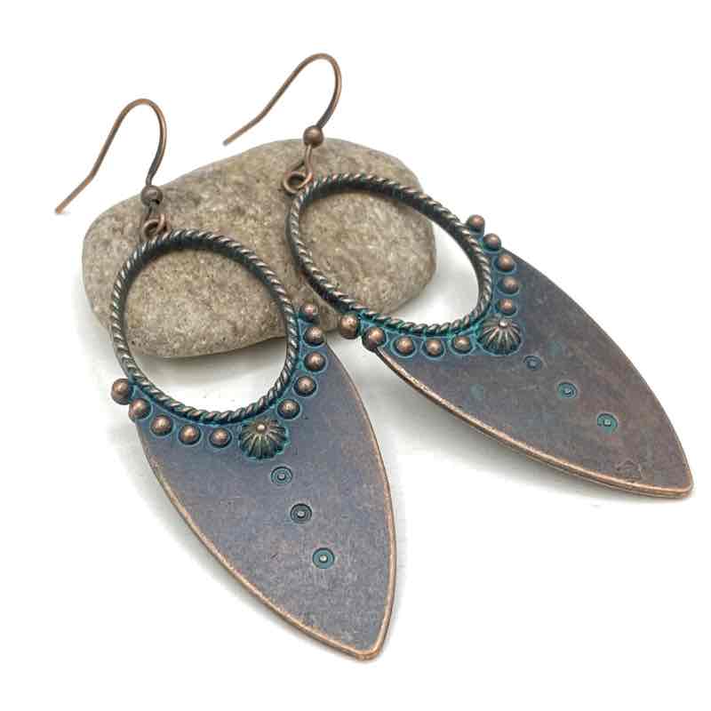 Two oxidised earrings with teal accents and a dual-tone finish, resting on a small, light-colored stone against a dark background.