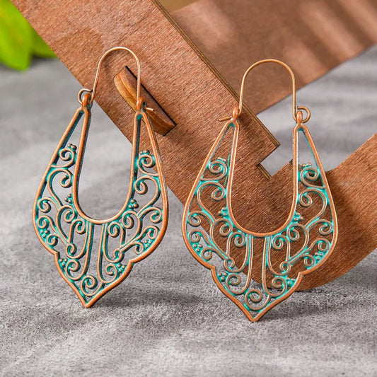 A pair of oxidised filigree drop earrings with a patina green finish, displayed on a wooden stand.