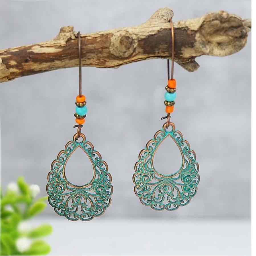 A pair of oxidised earrings with teal filigree teardrops and orange and turquoise beads, hanging from a tree branch.