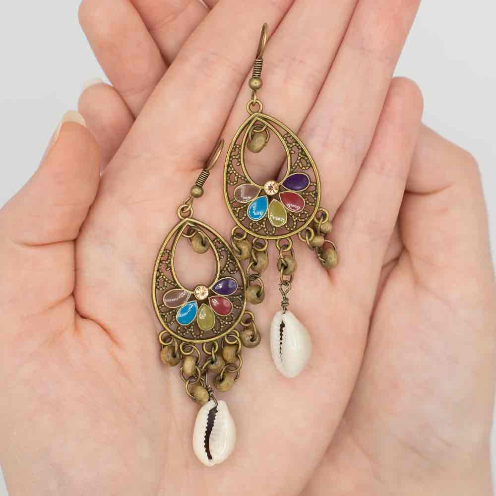 A pair of oxidised floral shell drop earrings with colorful enamel details, held gently in a person's hands.