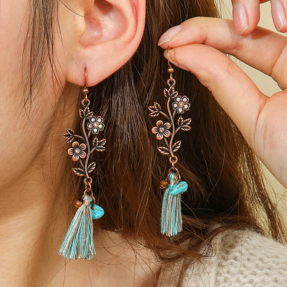 A person wearing oxidised floral tassel drop earrings with turquoise accents, holding one earring to show its detail.